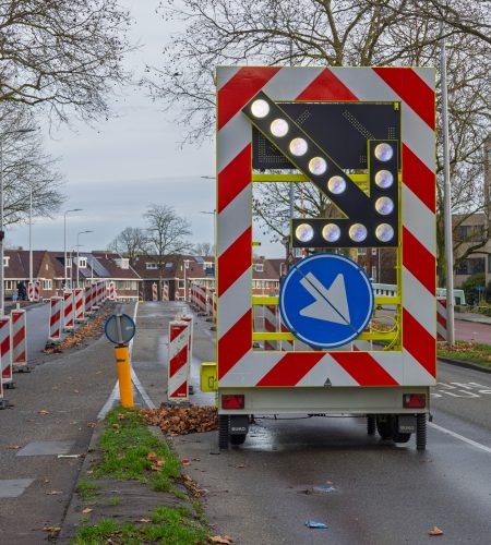 Mobile traffic warning trailer with an illuminated LED arrow and chevron patterns directing traffic during road construction in the Netherlands.